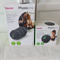 Photo of both sealed boxes for Beurer PhysioLine MG 35 Deep Roll vibrating massage roller and MG 10 vibrating massage ball together on a white surface.