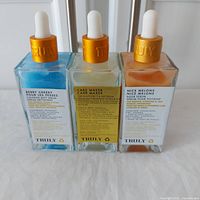 Three Truly brand serums in glass dropper bottles with gold tops: Berry Cheeky, Cake Maker, Nice Melons. The bottles contain different colored liquids: blue, clear, orange.