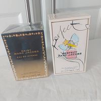 Two boxed Marc Jacobs fragrances side by side, Daisy Eau So Intense on left with navy to gold gradient box and Perfect on right with white artistic box, both sealed in cellophane.