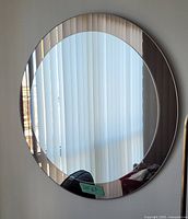 Front view of large round mirror showing two-tone glass and vertical blinds reflection.
