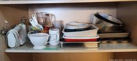 Wide view of kitchen shelf with various baking pans, bowls including metal bowls, ceramic dishes, and measuring cups