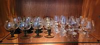 Overall view of vintage glassware including etched brandy snifters with green stems and clear wine glasses on wooden shelf