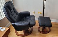 Side view of black leather swivel recliner and ottoman showing overall shape and wooden base