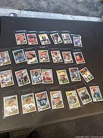 27 football trading cards arranged in rows on a table, showing front player images with bright borders and team logos, cards in mostly good condition.