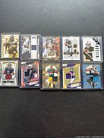 Photo showing 10 football trading cards with jersey patches in protective sleeves laid on a dark surface.