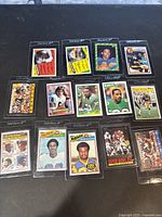 Top view of 13 Topps football trading cards in protective sleeves arranged on a black surface.