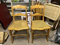 Two antique birdseye maple wooden chairs with woven cane seats, showing front view with one cane seat intact and one damaged and needing repair.