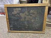Front view of antique wooden chalkboard showing peeling chalkboard paint and some chalk markings on the surface, surrounded by a solid oak wood frame.