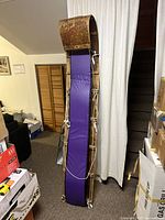 Photo showing full length of antique wooden toboggan with curved front and purple fabric pad against a beige curtain.