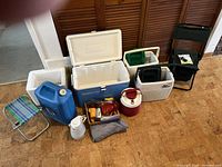 Wide shot showing all items including coolers, chairs, water containers, kettle, lantern, and camping accessories