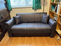 Dark gray patterned fabric IKEA liveseat sofa bed with two cushions, pictured in living room setting from left angle. Visible damage is not apparent on fabric surface.
