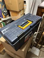 Dark blue plastic Mastercraft toolbox with yellow handle placed on cardboard boxes in a storage area