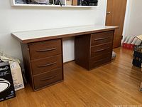 Full view of the desk showing the overall structure, wood finish, white laminate top, and drawer arrangement.