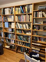 Front view of three bookshelves filled with books, showing the light pine veneer finish and seven shelves each.