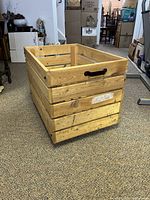 Side view showing the wooden slat construction, black metal handle, and rollers underneath the bin