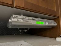 Under cabinet mounted Sony ICF-CDK50 FM/AM CD clock radio showing front view with illuminated green digital display and control buttons.