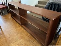 Side and front view of the dark walnut wood veneer bookshelf placed on wooden floor near stairs and furniture