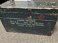Front and top view of the vintage black wooden box with white stenciled text specifying RCAF radio transmitter receiver container details.