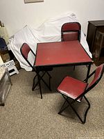 Square folding card table set with four folding chairs, red table top and red vinyl upholstery on chairs, black metal frames