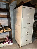 Front side view of the vintage wooden filing cabinet showing all four drawers and metal handles, painted cream with wear and scratches.