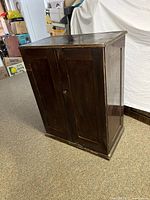 Full view of closed vintage wooden storage cabinet showing brown wood finish and paneled front doors.
