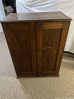 Front view of the vintage walnut wooden storage cabinet with closed double doors, showing minor surface scratches and wear.