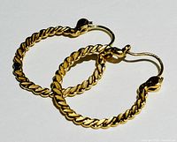 Pair of yellow gold twisted loop hoop earrings lying flat on a white background, showing the overall twisted pattern and latch backs.