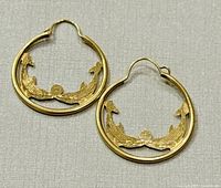 Pair of 10K yellow gold loop earrings on white fabric background showing the full front view with decorative motifs visible.