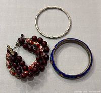 Three bracelets displayed from above; two cloisonne bangles and one red beaded bracelet.