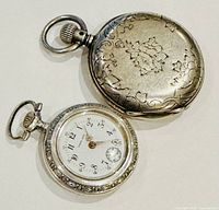 Overview of two silver pocket watches: one closed hunter-case with floral engraving and one open-face Arabic numeral dial watch.