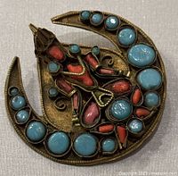 Front view of antique Tibetan brooch showing detailed seated Buddha made with red coral and turquoise in a brass crescent frame.