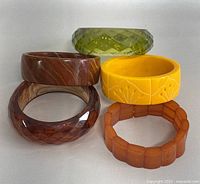 Five carved Art Deco Bakelite bangles in different colors and styles shown stacked and individually.