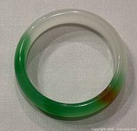 Top-down view of the natural jade D-shaped bangle showing green and white color gradient with minor brownish area.