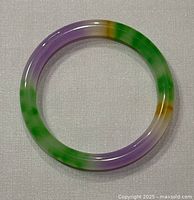 Top-down view of the natural jade bangle showing smooth rounded edges and mixed shades of purple, green, and amber.