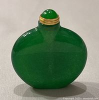 Front view of the green jade bottle with gold accents on the stopper and neck, showing rounded flattened shape.