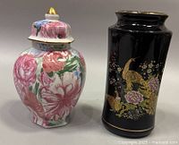 Both items shown: black cylindrical vase with gold peacock design and floral ginger jar with lid decorated with pink and red flowers.