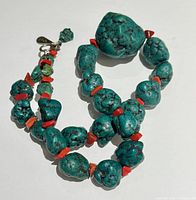 Full view of the necklace laid out showing the large turquoise nugget bead center and alternating smaller turquoise and red coral beads with clasp detail.