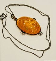 Front of oval amber cabochon pendant with silver bezel and decorative loops