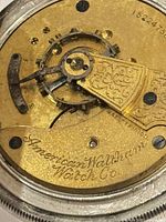 Close-up photo of the watch's mechanical movement showing the engraving 'American Waltham Watch Co.' on a gold-toned component with intricate design.