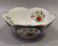 Side view of Lotus shaped ceramic bowl showing scalloped edges, gold trim, and hand painted Imari floral motifs with red lotus flowers and small colorful architectural details.