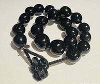 Coiled black bead prayer tasbih showing beads, braided cord, metal tag, and carved flower pendant