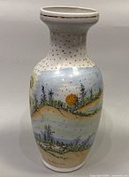 Full front view of the 10" white porcelain vase with raised gold dots on neck and hand painted landscape scene on the body