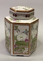 Front and side view of hexagonal ceramic jar showing hand painted hummingbirds and lotus flowers with gold border accents.