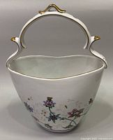 Front view of the white porcelain basket showing floral pattern and handle with gold detailing.