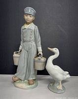 Front view of both figurines; person holding two buckets and white duck.