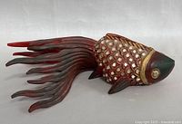 Side view of hand carved and painted koi fish showing detailed scales, painted eyes, flowing tail, and fins.