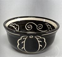 Front and side angle showing the black ceramic bowl with white abstract floral motifs and slight rim wear.