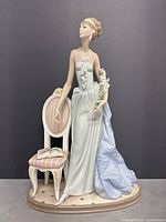 Full view of the figurine standing beside chair on oval base against dark background