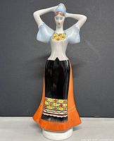 Front view of porcelain figurine showing detailed hand-painted traditional dress with flower motifs and orange skirt.