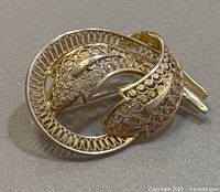 Close-up image of the front of the brooch showing the intricate filigree leaf-like design and circular frame.